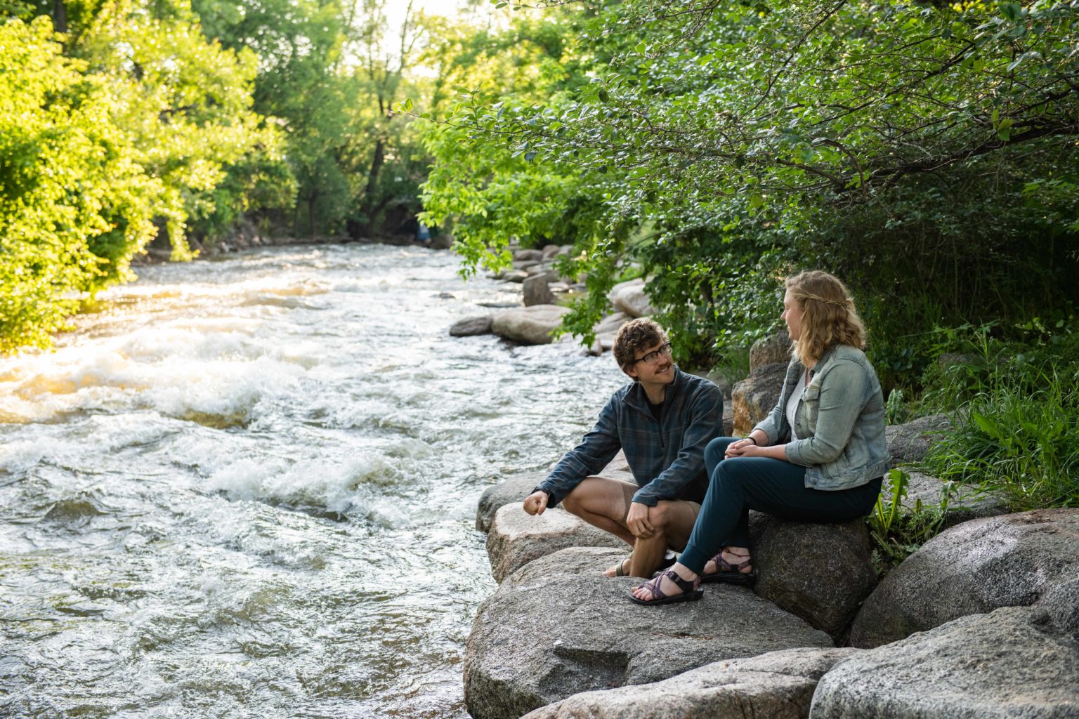 A couple sitting and talking next to a rushing stream.