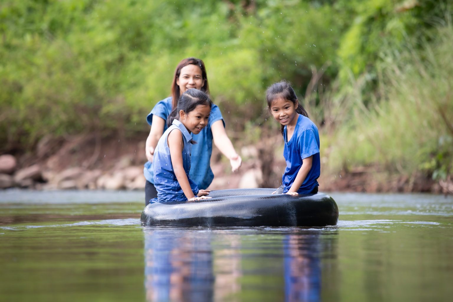 A woman pushes two children on an innertube down a stream.