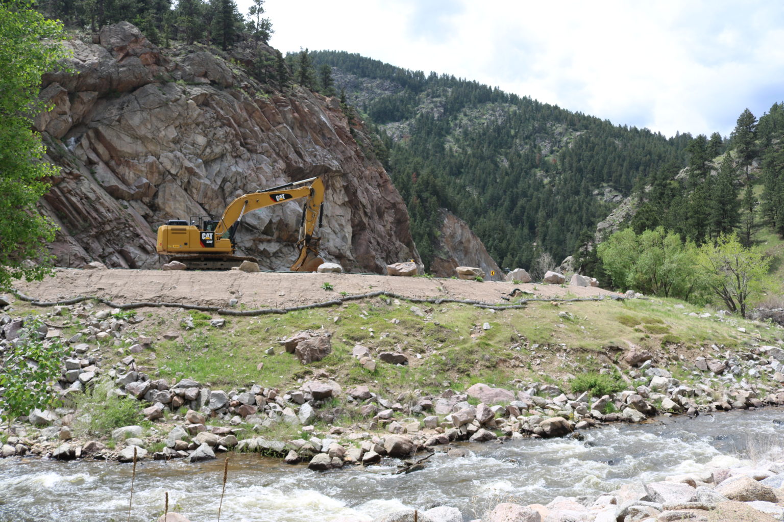An excavator works near a rushing river.