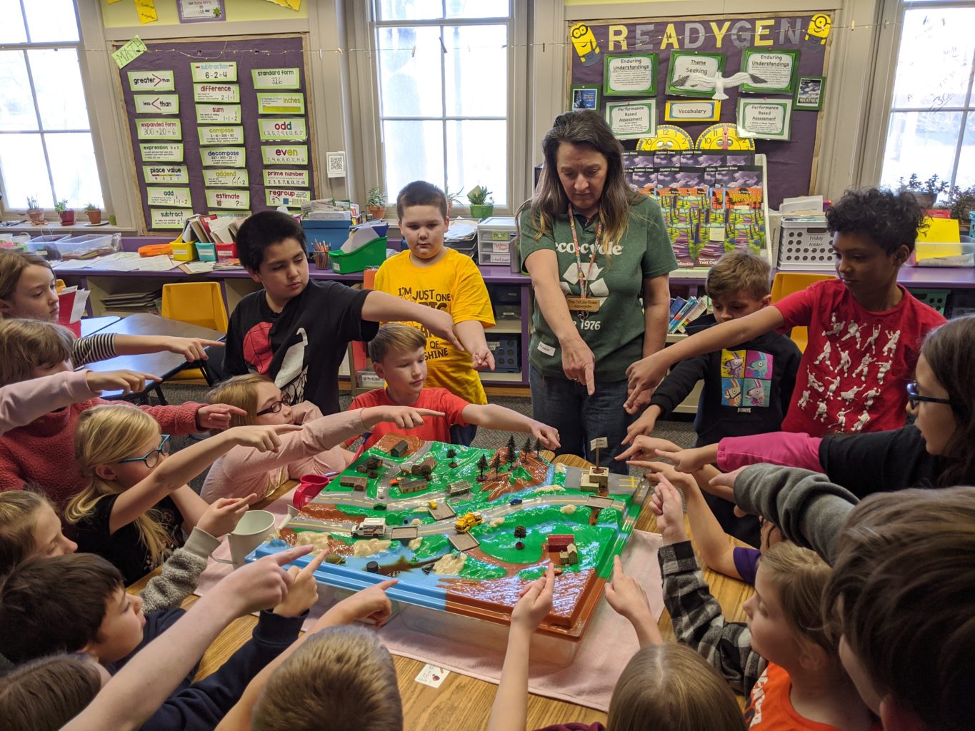 A teacher and classroom of students point to a watershed model.