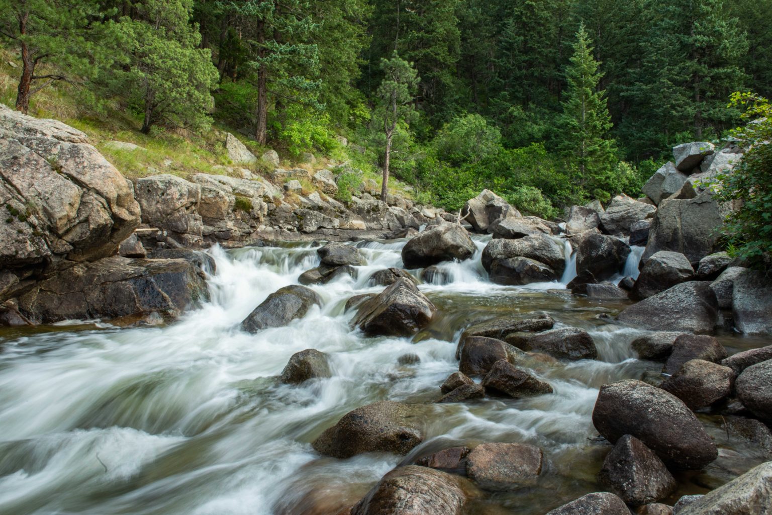 Water flows down a wide creek full of rocks, appearing as a series of small waterfalls.