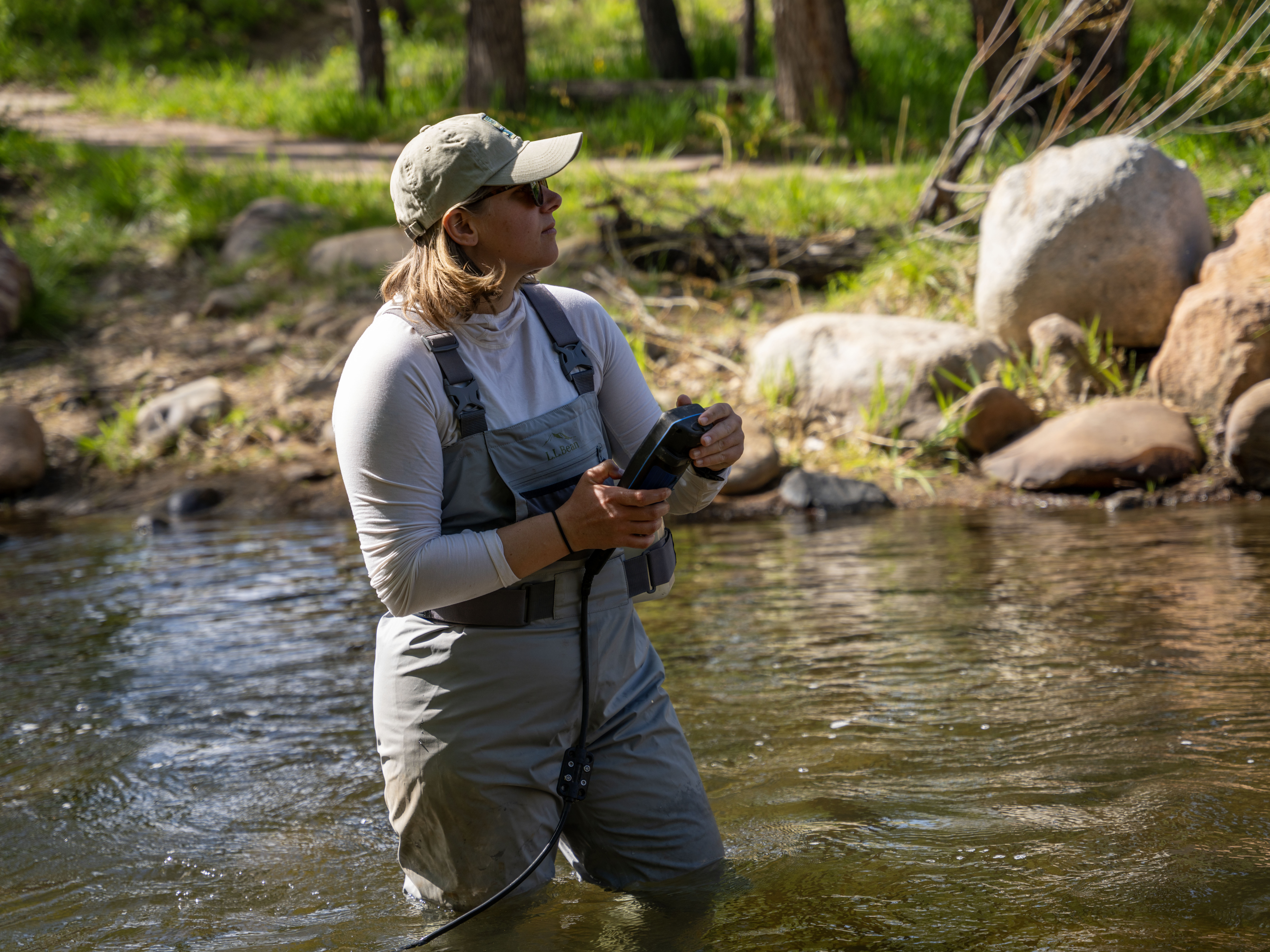 A woman in waders stands in a creek using a water quality monitoring tool.