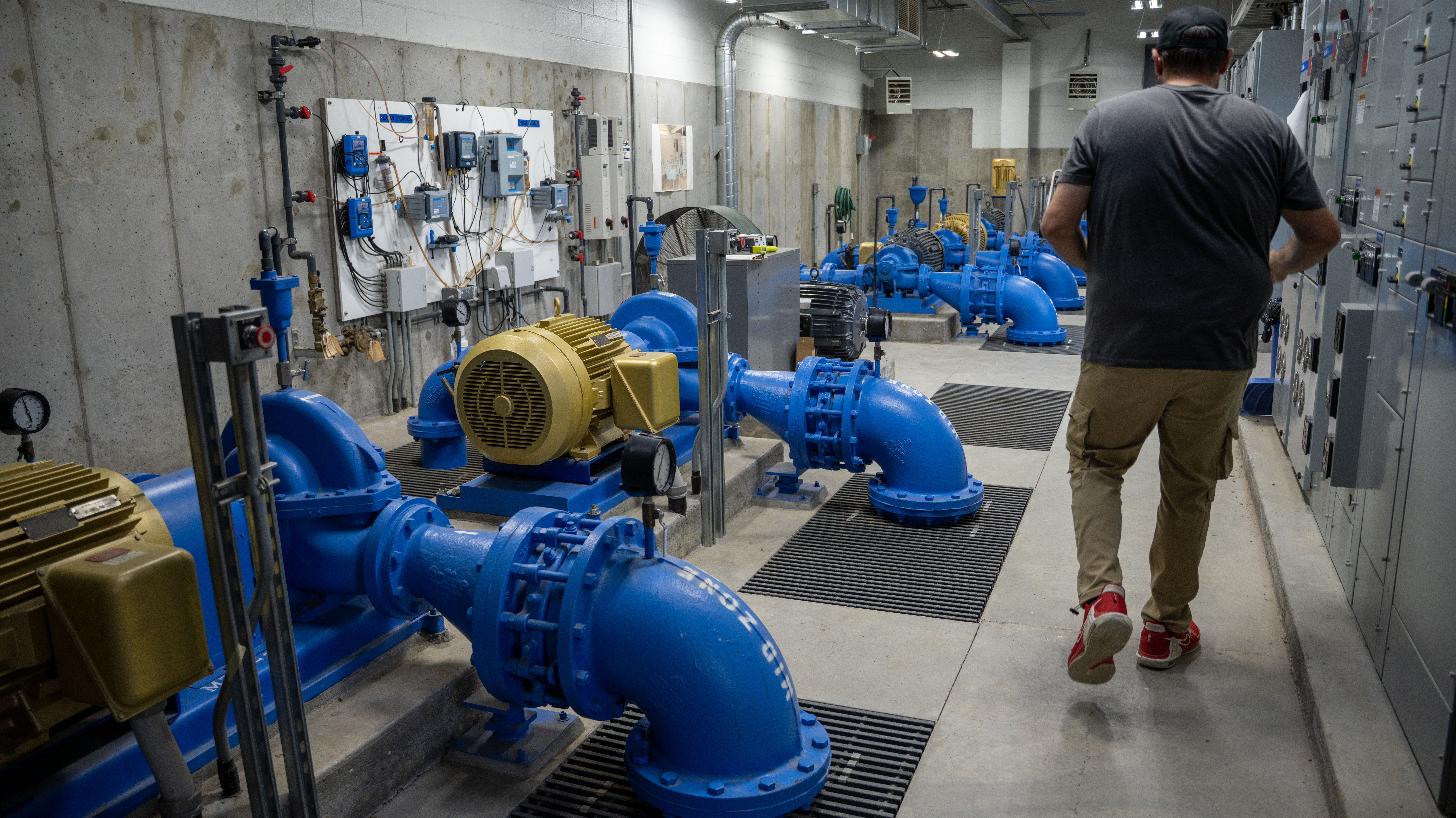 A man walks through a room filled with large blue pipes and other machinery.