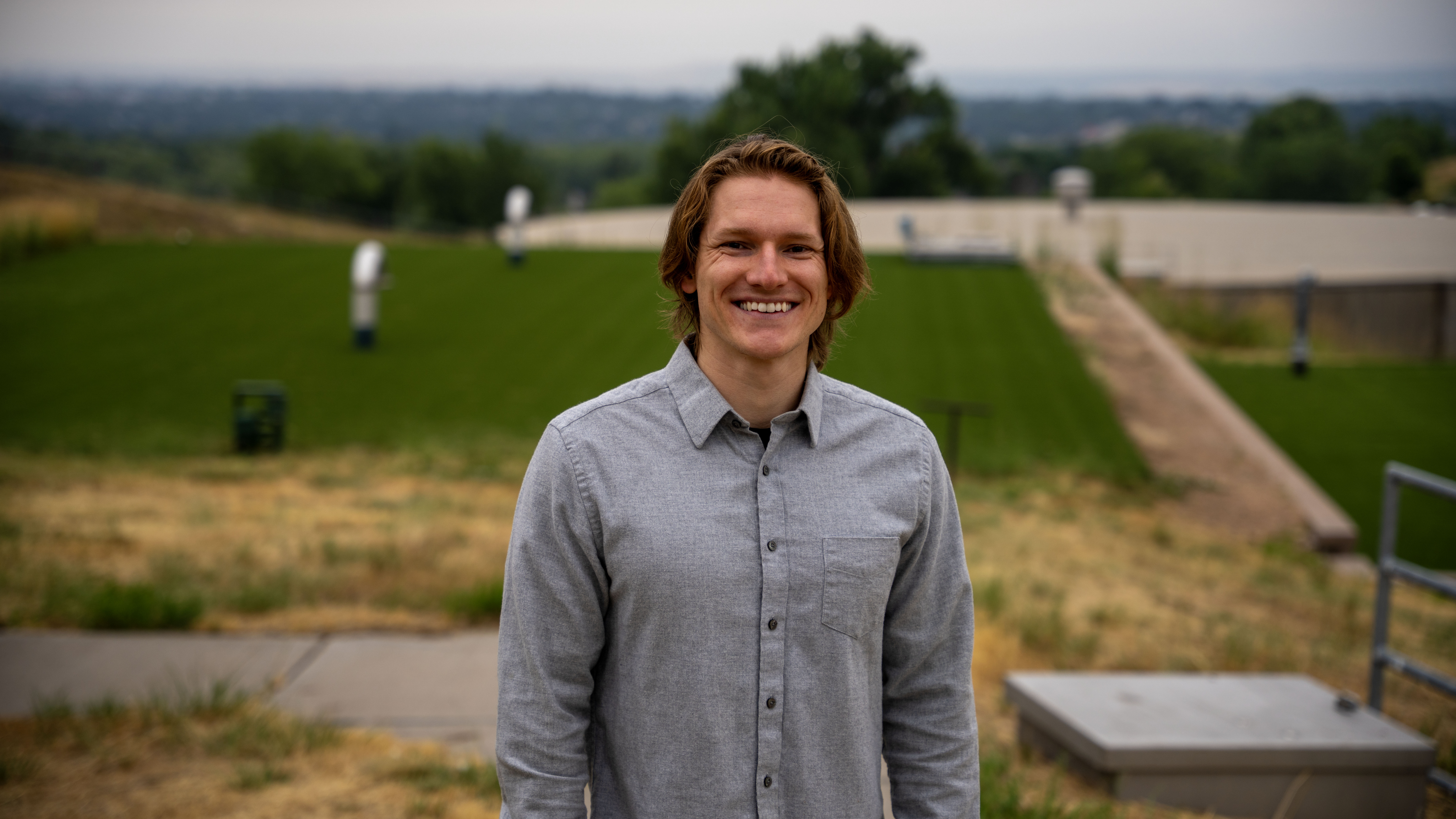 A man stands smiling with water treatment facilities in the background.