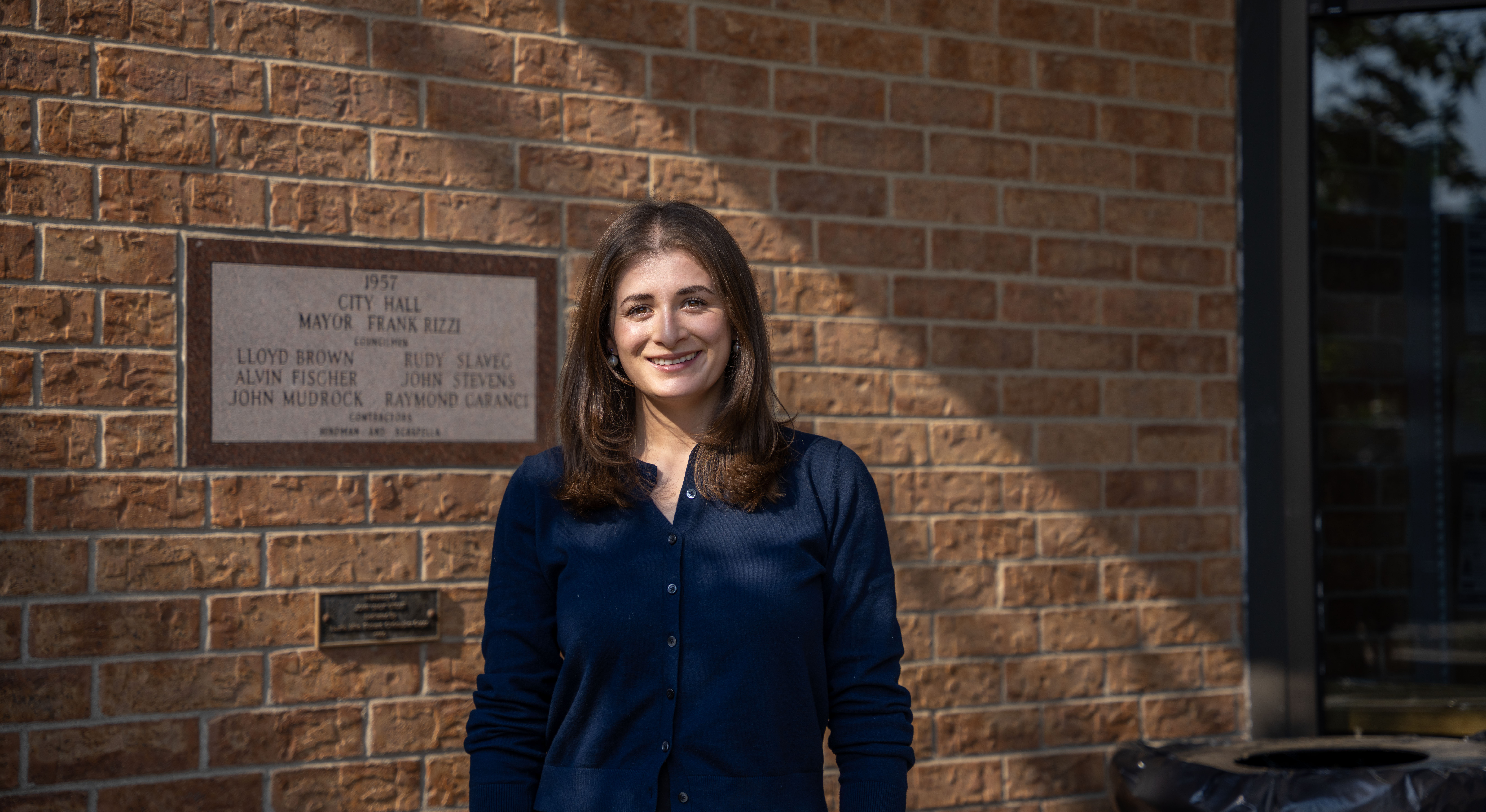 A smiling woman stands outside a brick municipal building.