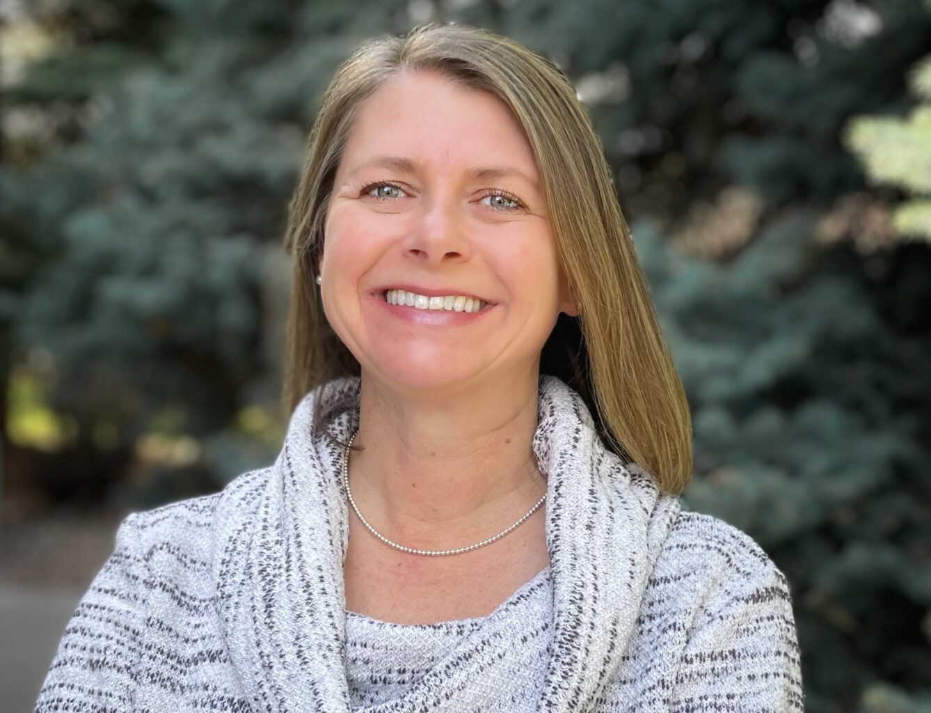 Headshot of a smiling woman standing in front of trees.