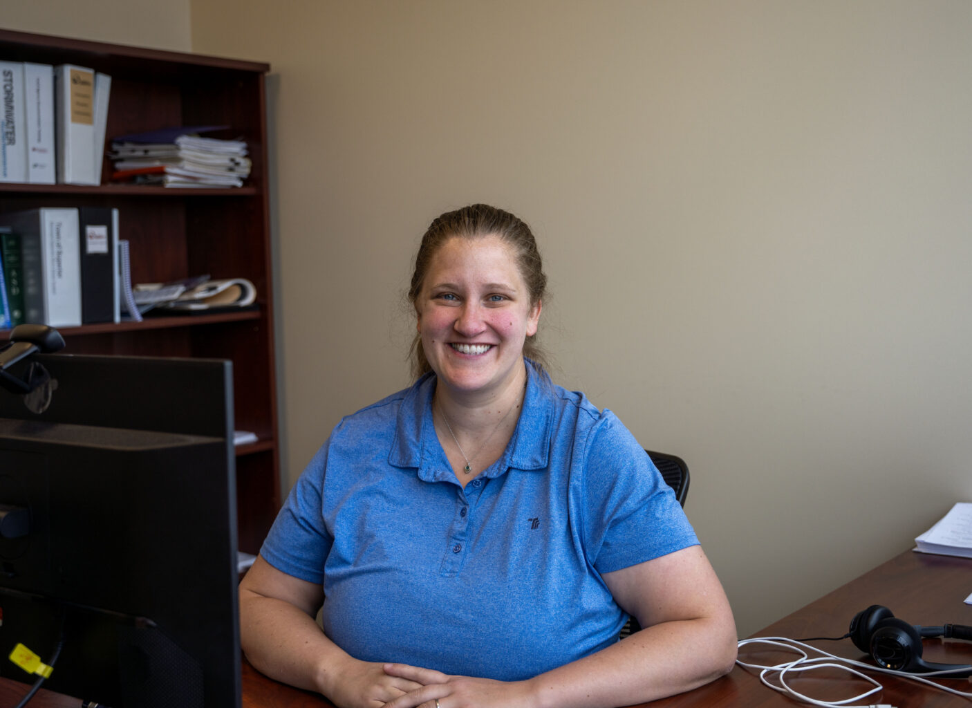 A smiling woman sits at a desk in an office.