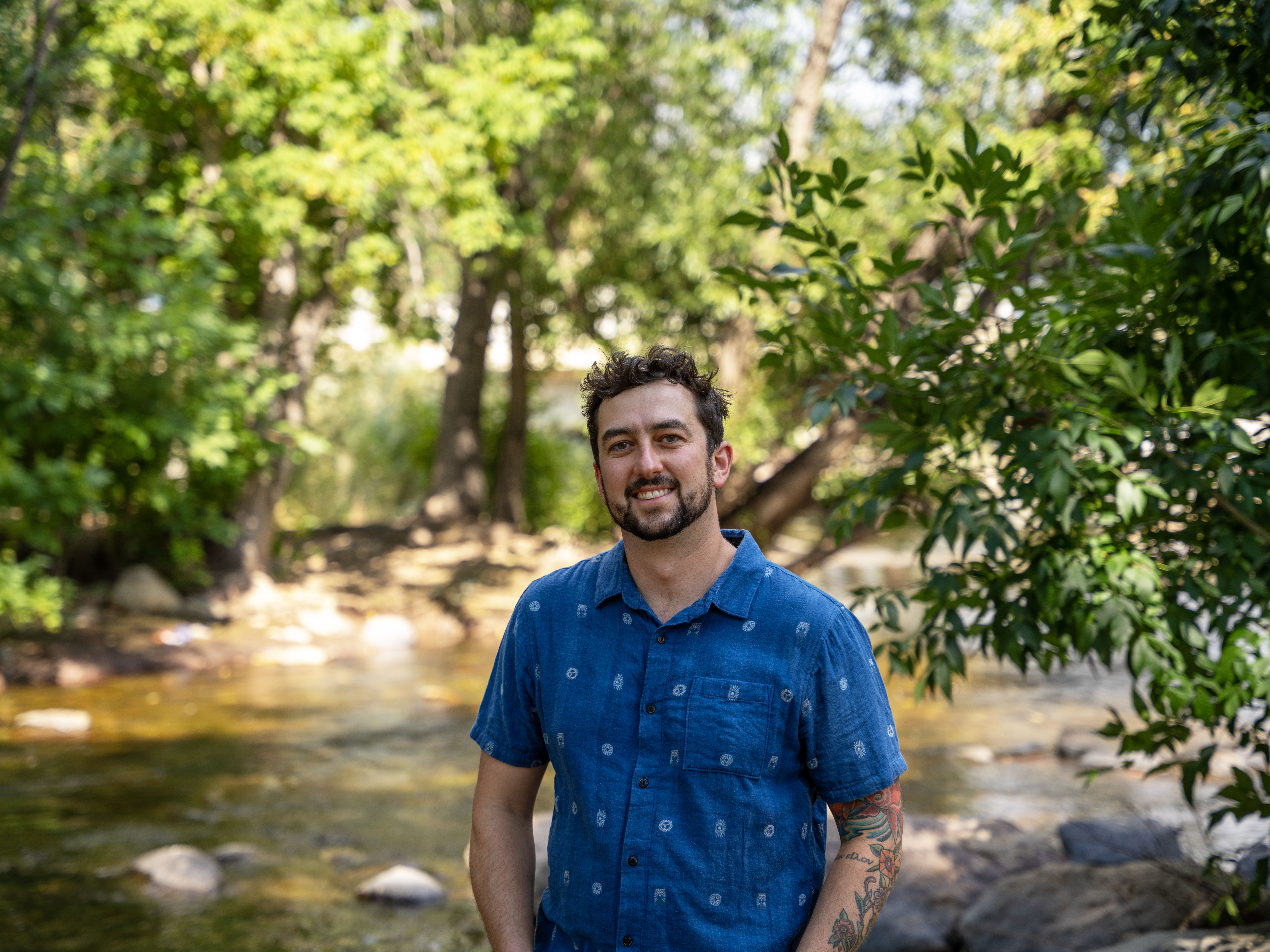 A man stands in front of a shaded river.