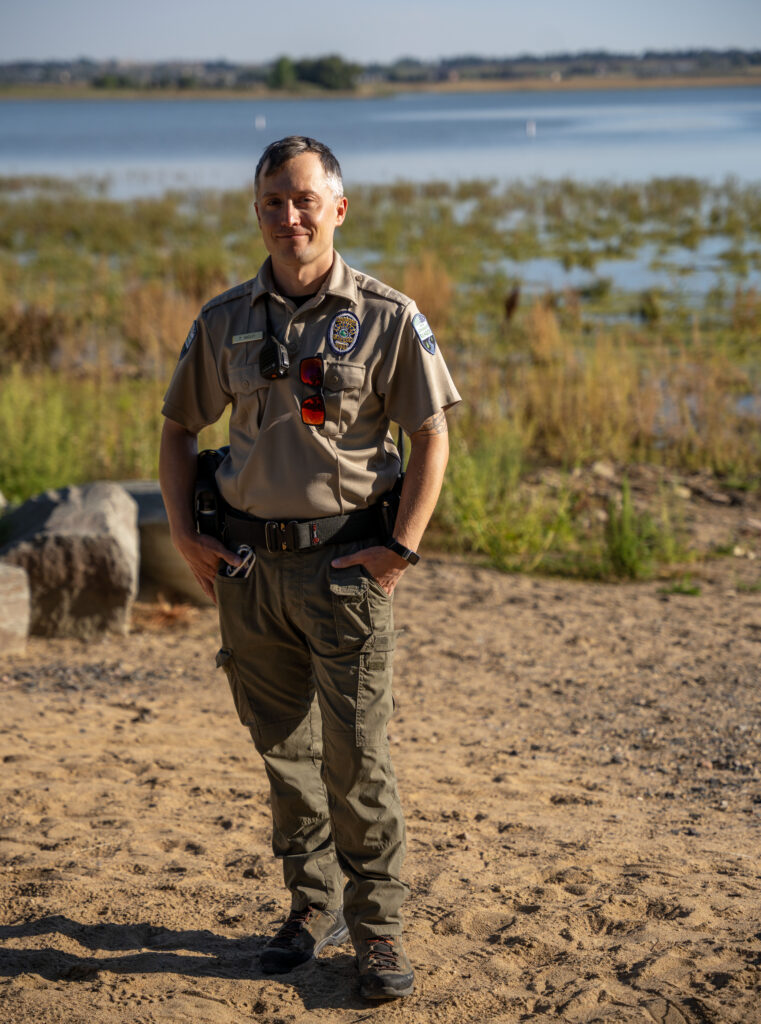 Man in law enforcement uniform stands in front of a reservoir.