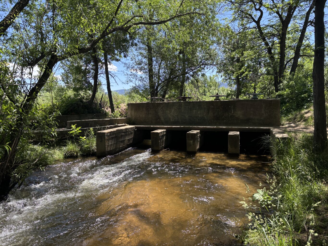 A concrete structure with slots that can be made larger or smaller sits across a shallow stream to divert water.